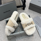 Pair of cream shearling sandals with tan side straps and black buckle details.