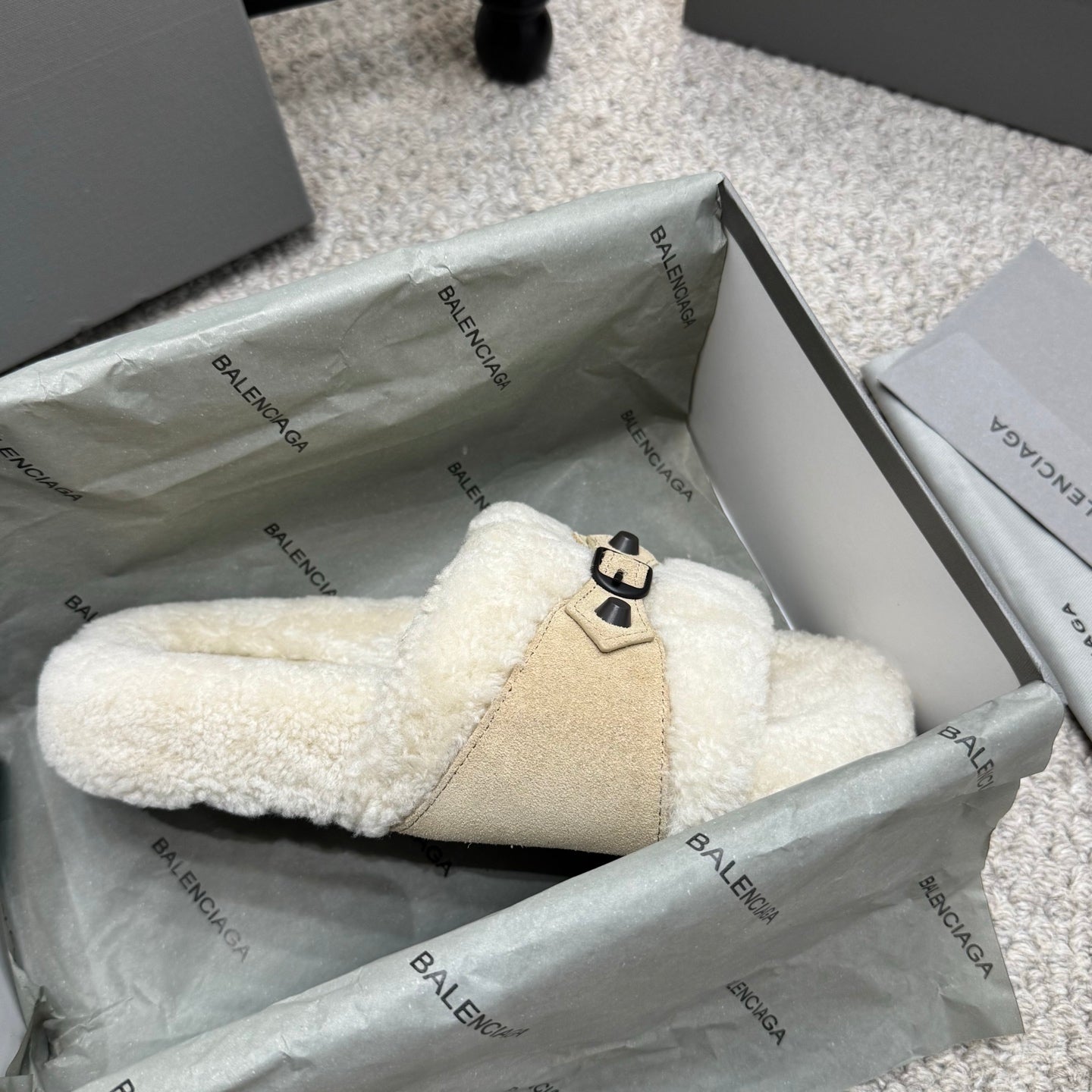Cream faux-shearling mule sandals with tan strap panel and black buckle detail.