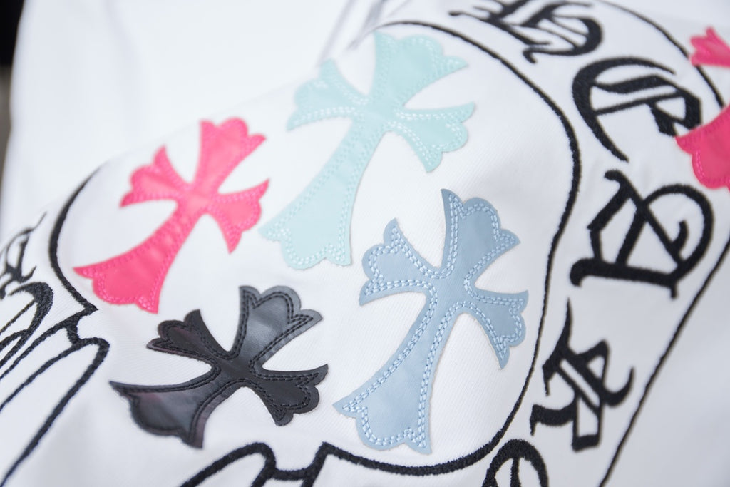 Close-up of circular crest graphic with pink and light-blue cross shapes on white tee