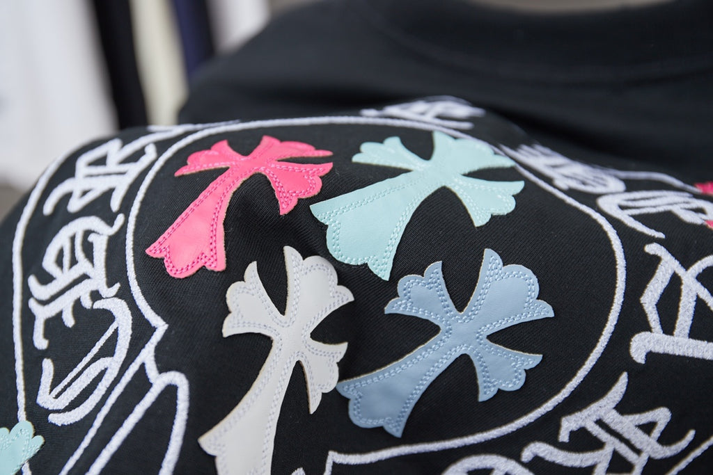 Black T-shirt logo close-up with pink and blue cross-shaped elements