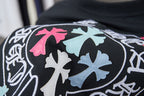 Black T-shirt logo close-up with pink and blue cross-shaped elements