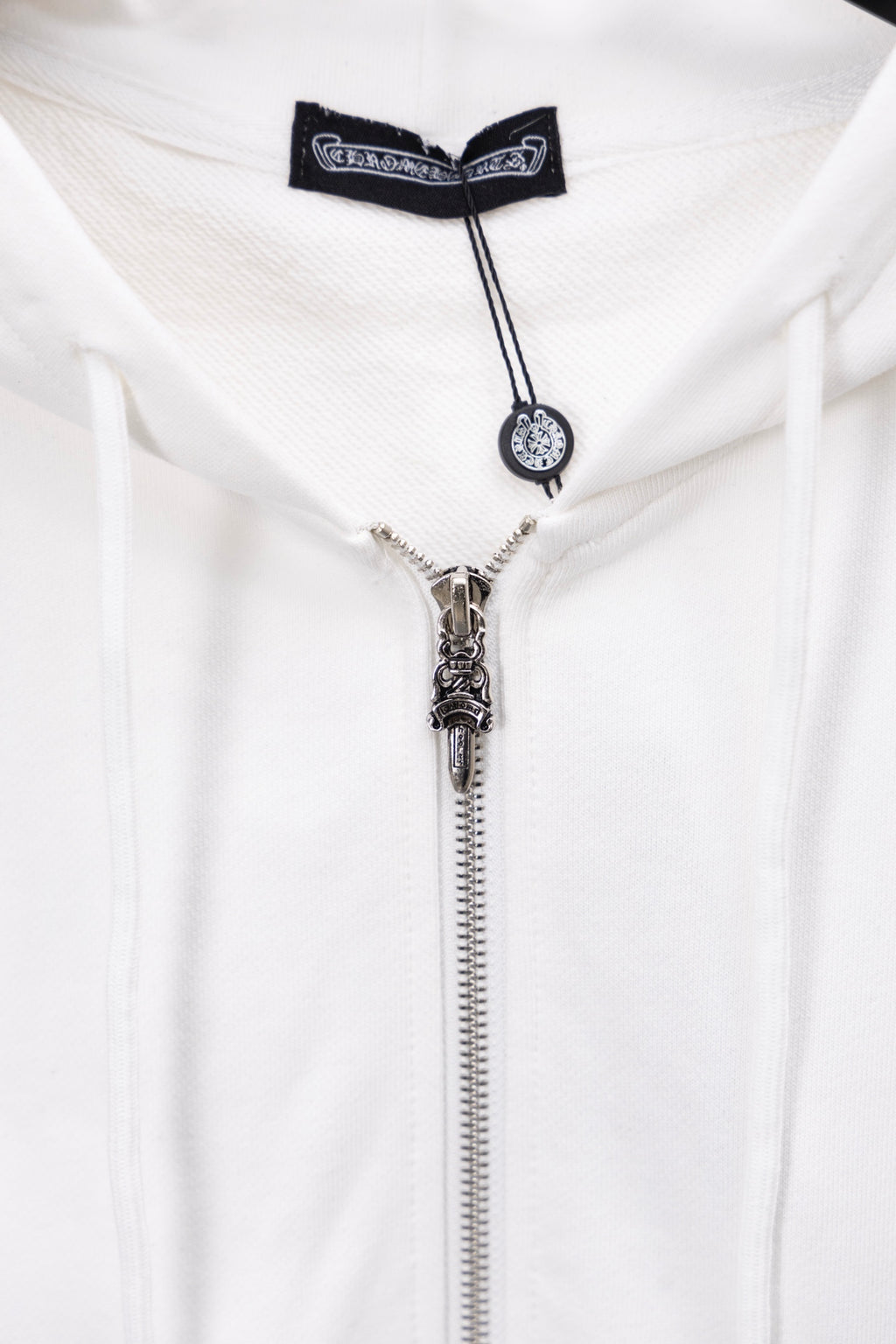 White zip-up hoodie close-up of metallic zipper pull and cord charm
