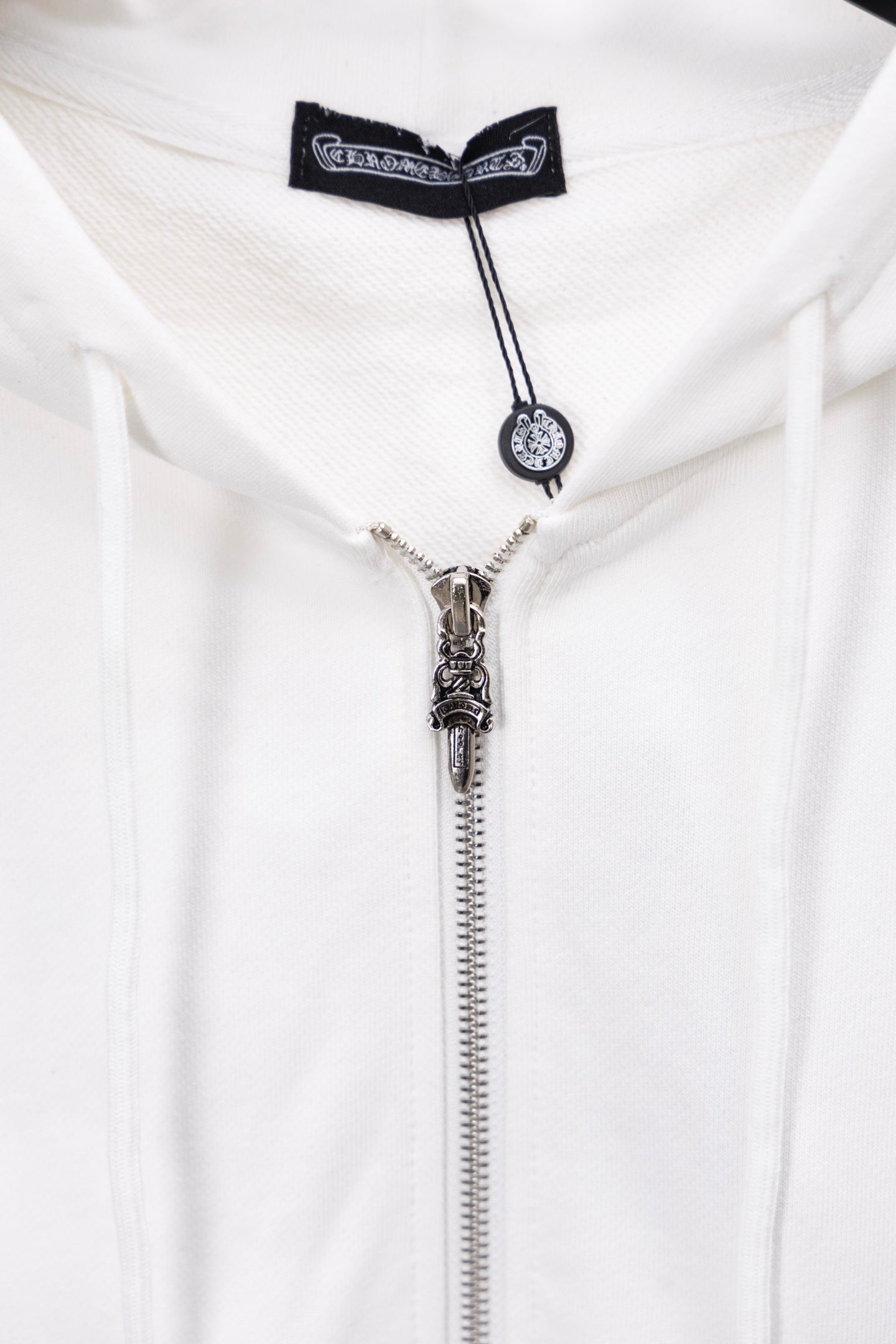 White zip-up hoodie close-up of metallic zipper pull and cord charm