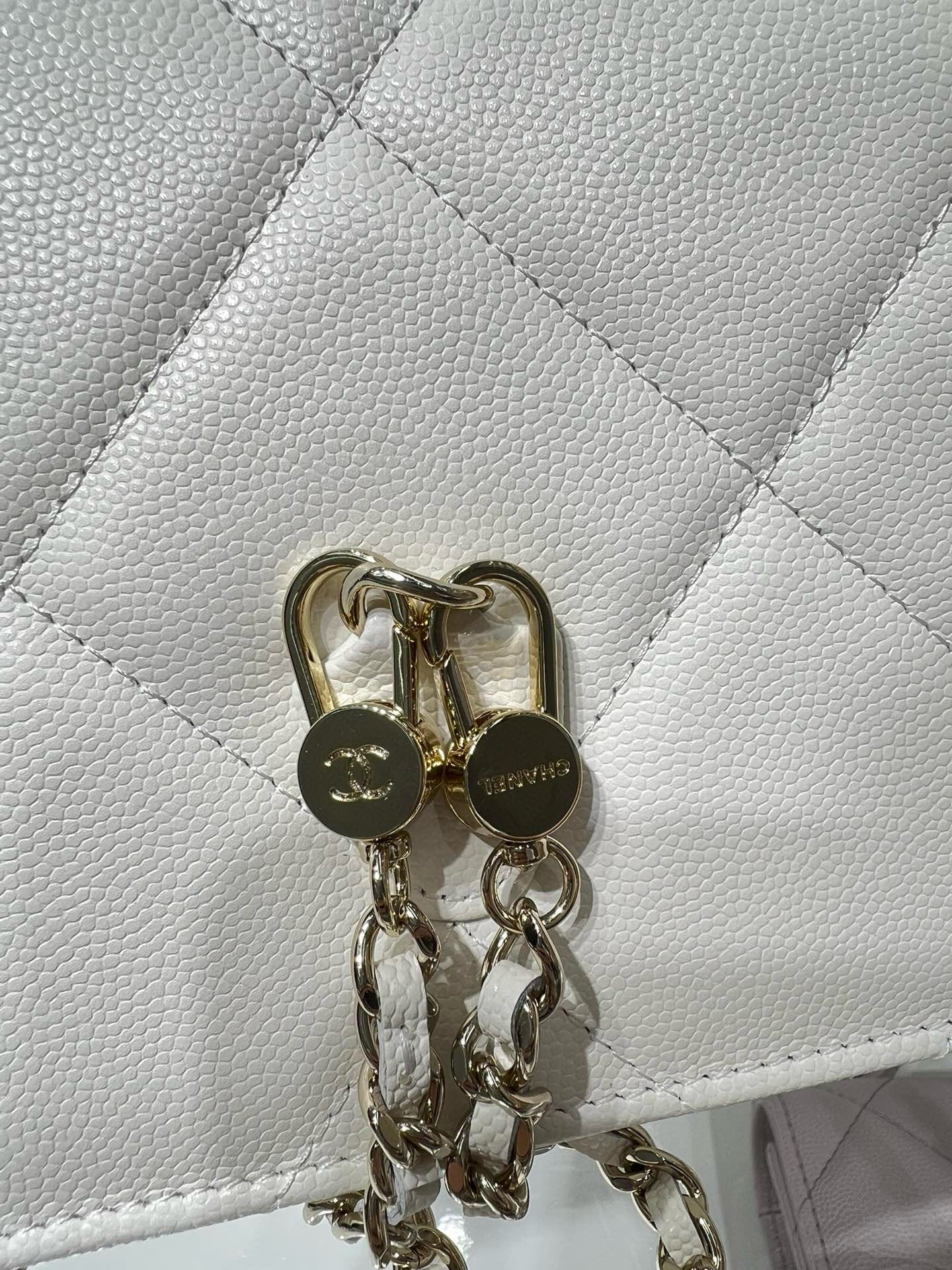 White quilted bag flap with gold ring pull hardware and attached chain links