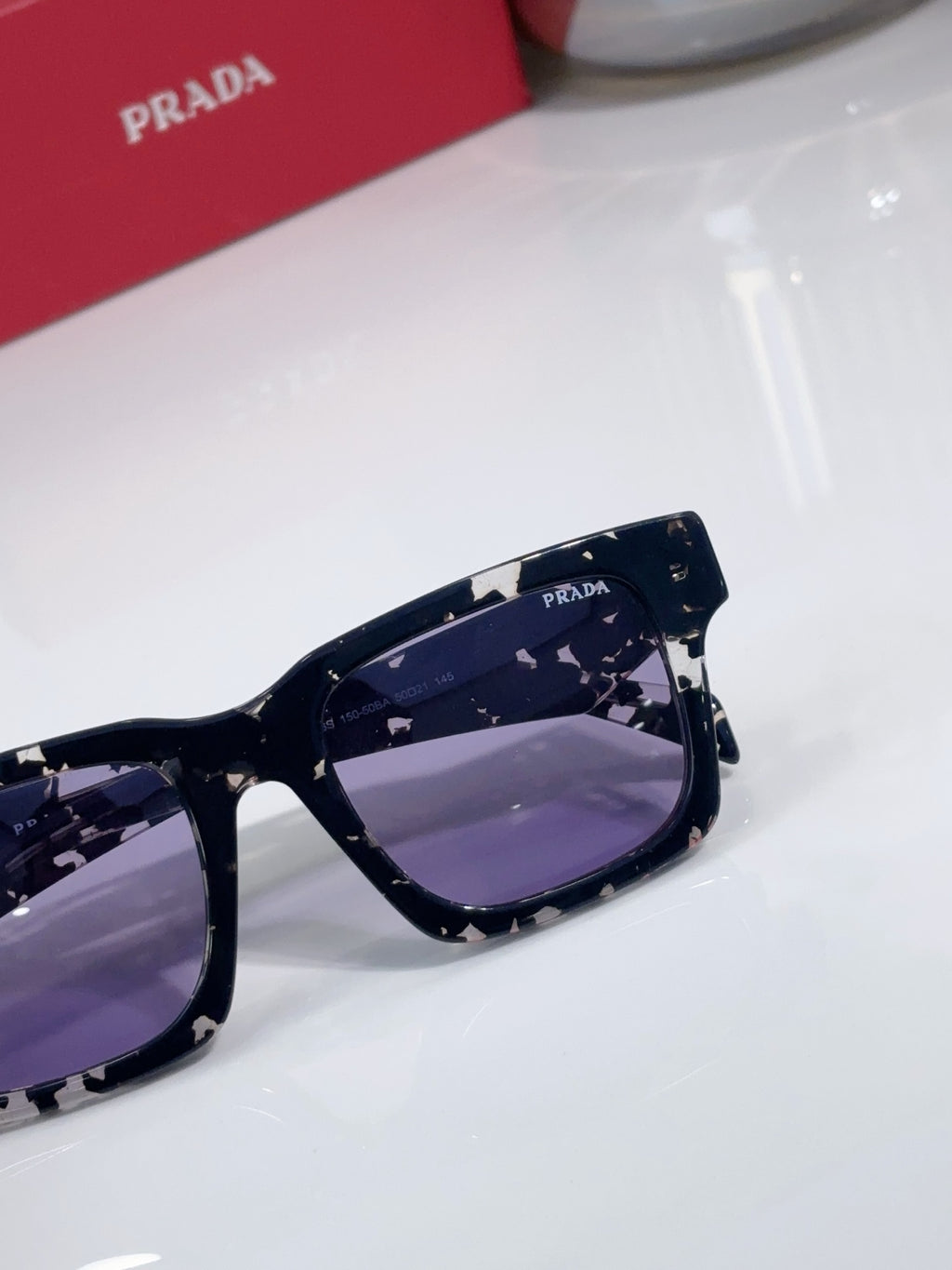 Prada square sunglasses close-up with navy patterned frame and purple-tinted lens