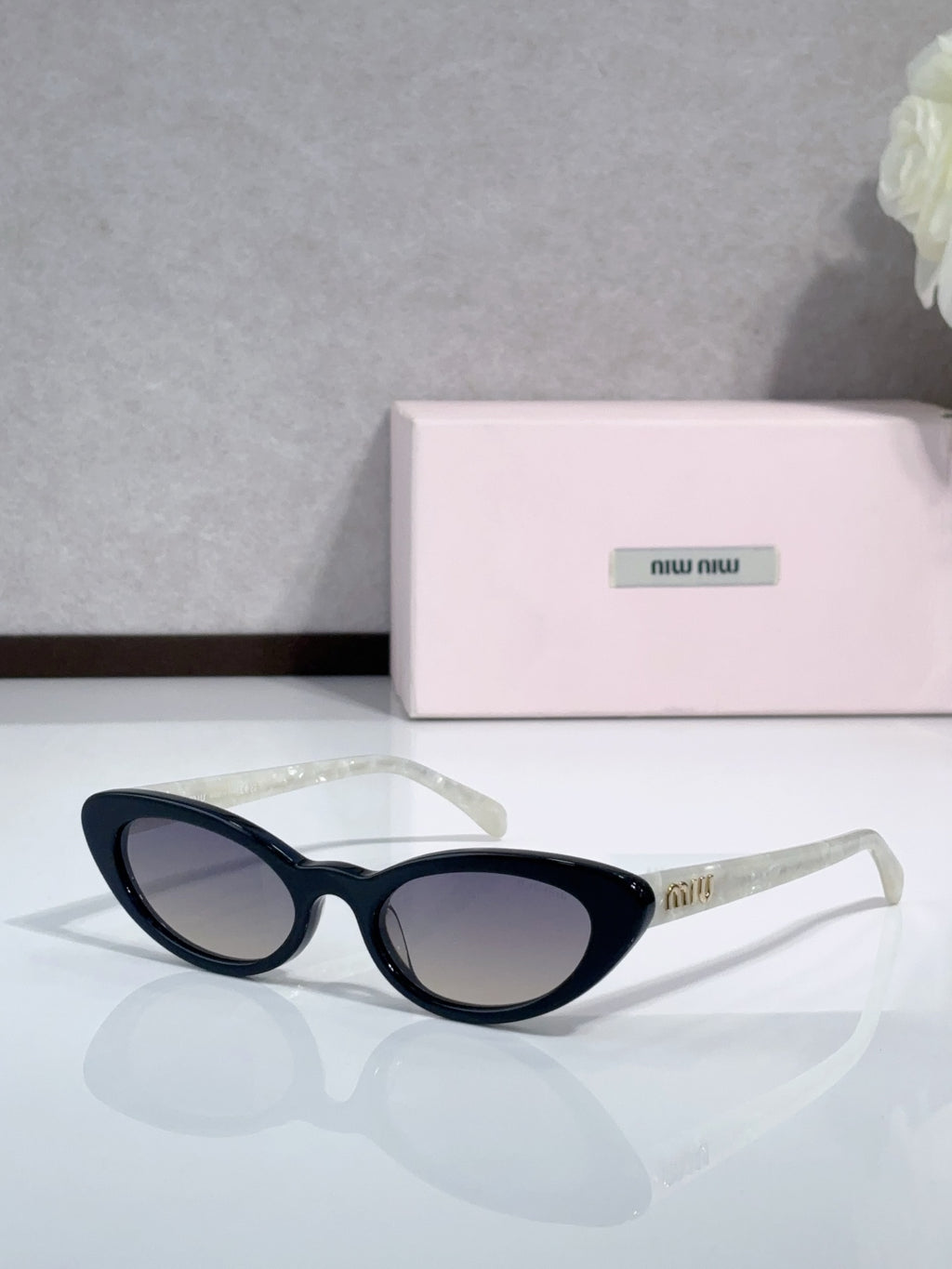Cat-eye sunglasses with dark lenses and black frames; logo on temple.