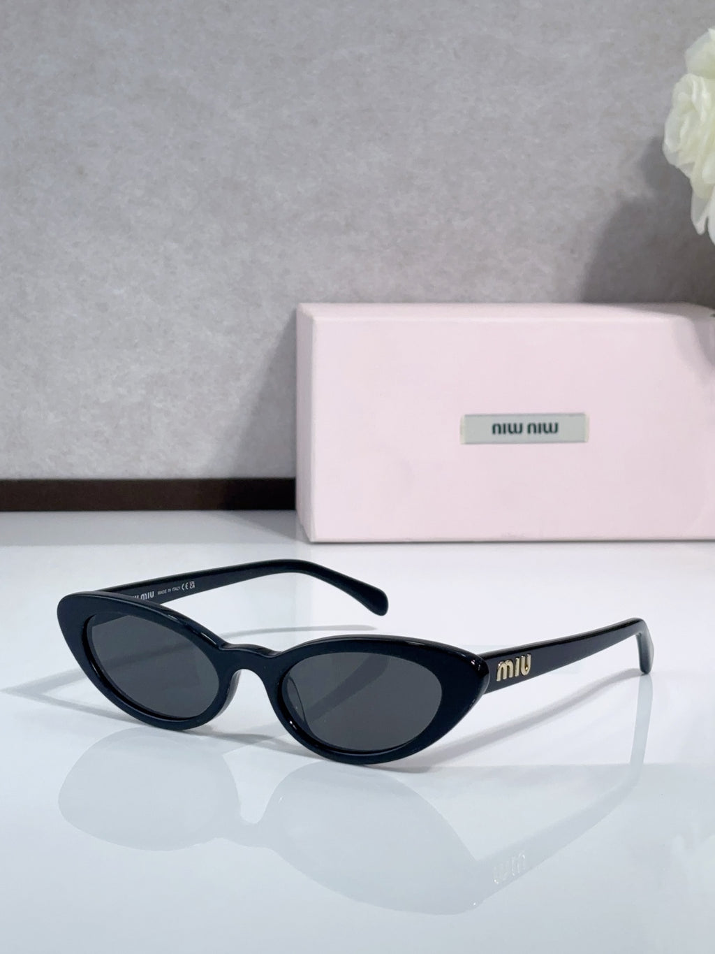 Cat-eye sunglasses with dark lenses and black frames; logo on temple.