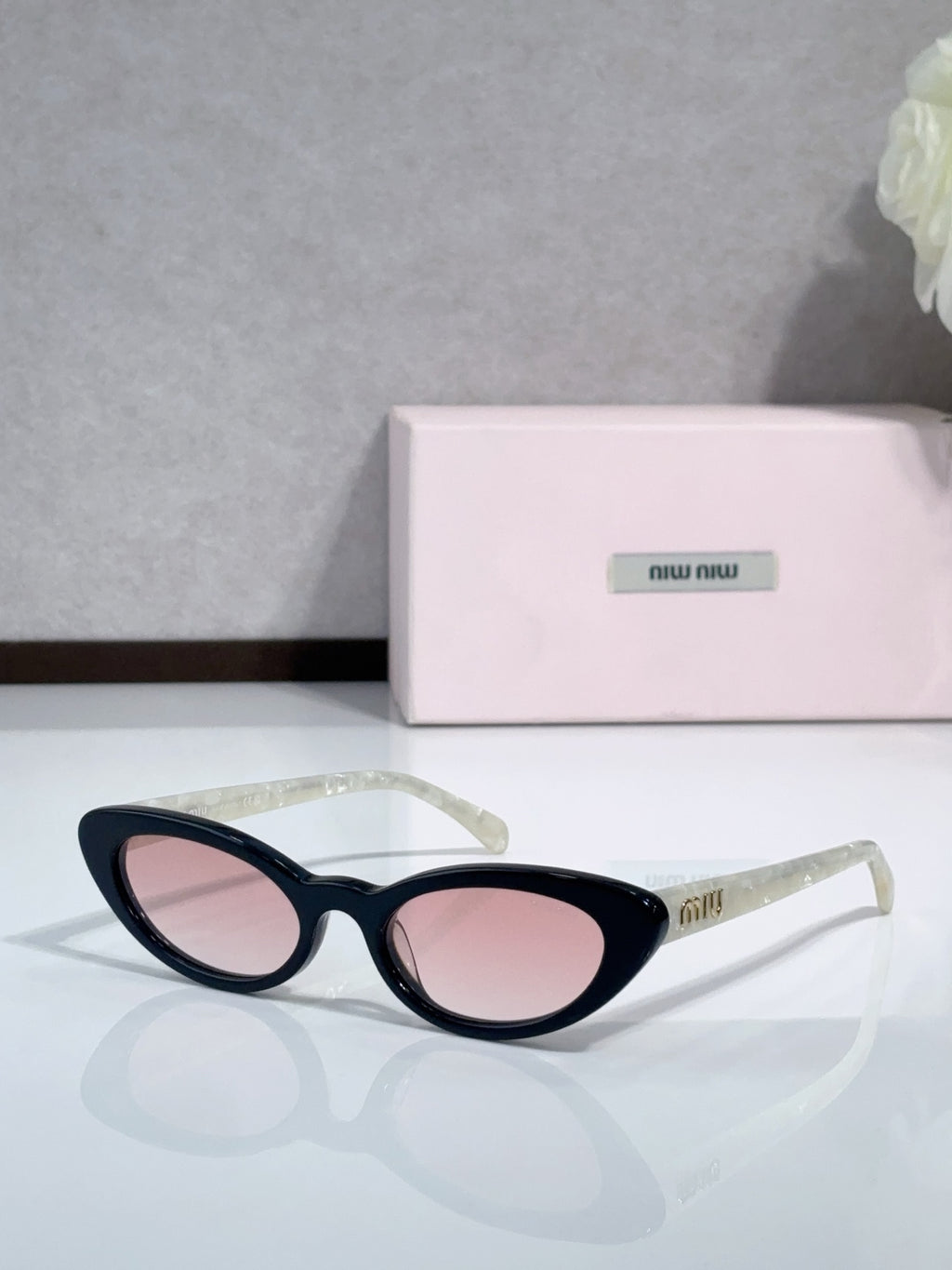 Cat-eye sunglasses with pink-tinted lenses and black frames; logo on temple.