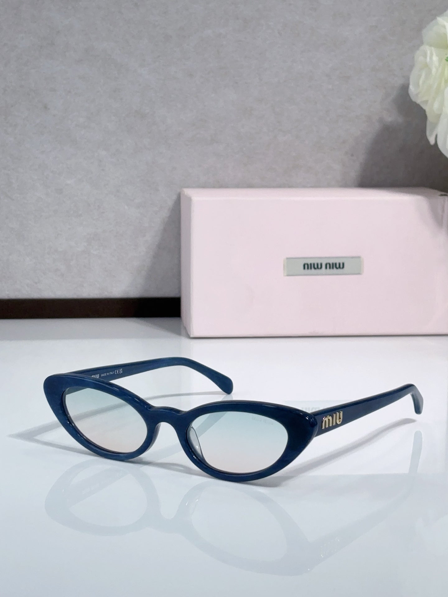 Cat-eye sunglasses with blue frames and clear lenses; logo on temple.