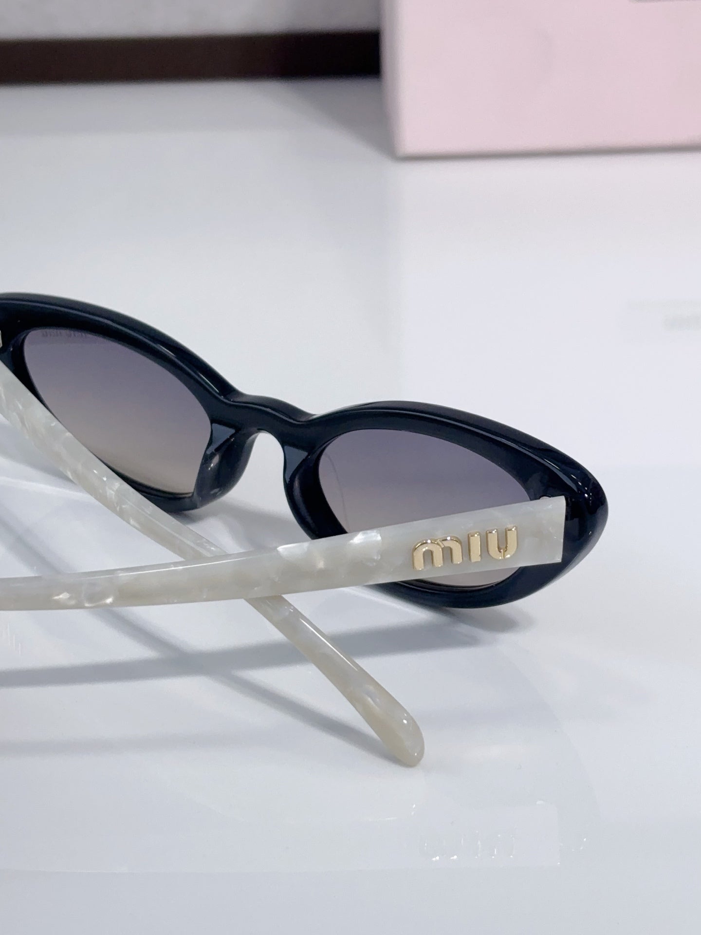 Close-up of cat-eye sunglasses with black frames and 'miu' logo on temple.