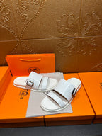 Hermes white slide sandals with two buckle straps, shown on a dust bag