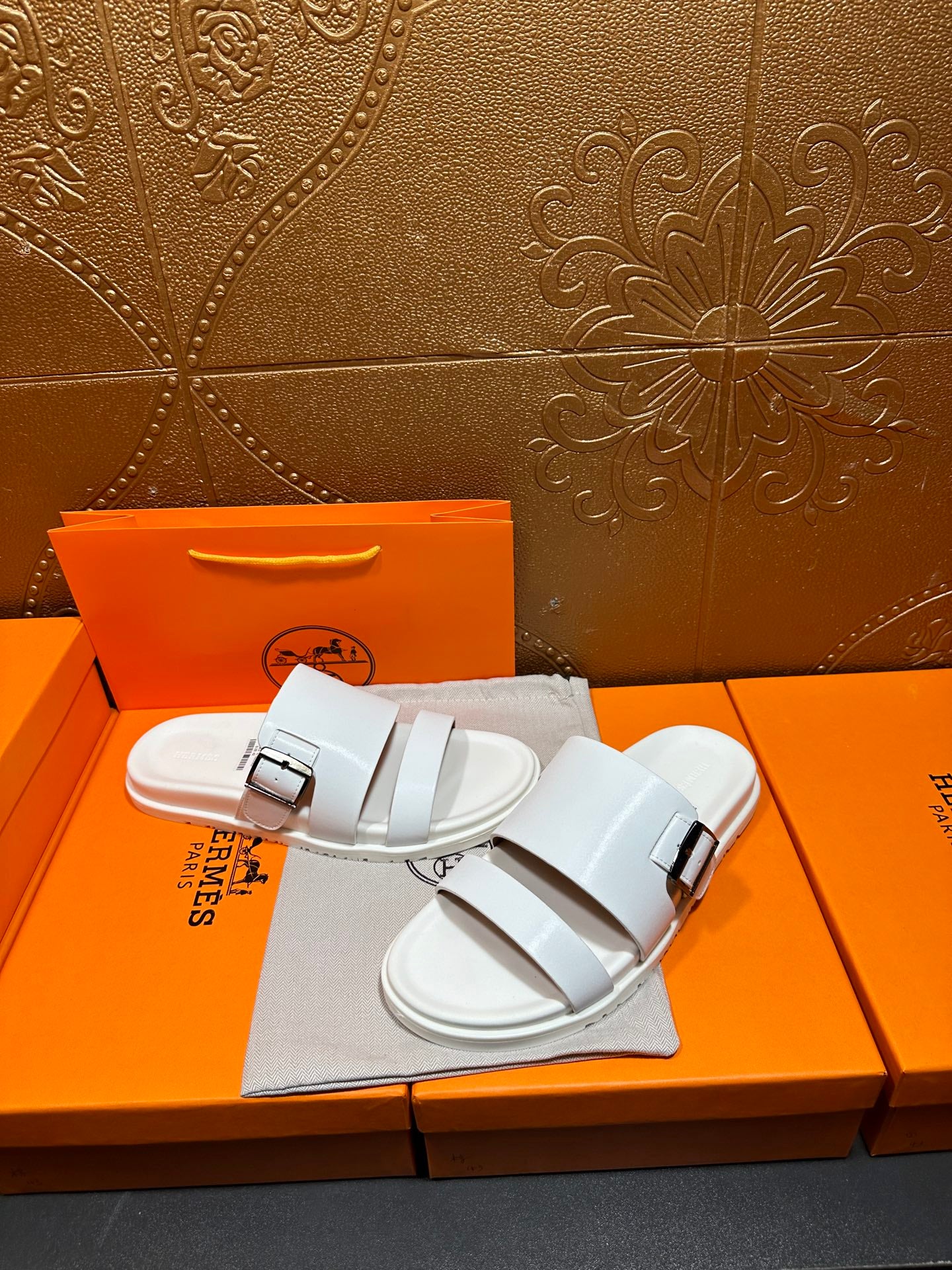 Hermes white slide sandals with two buckle straps, shown on a dust bag