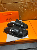Black leather slide sandals with two straps and buckle, top view pair on dust bag