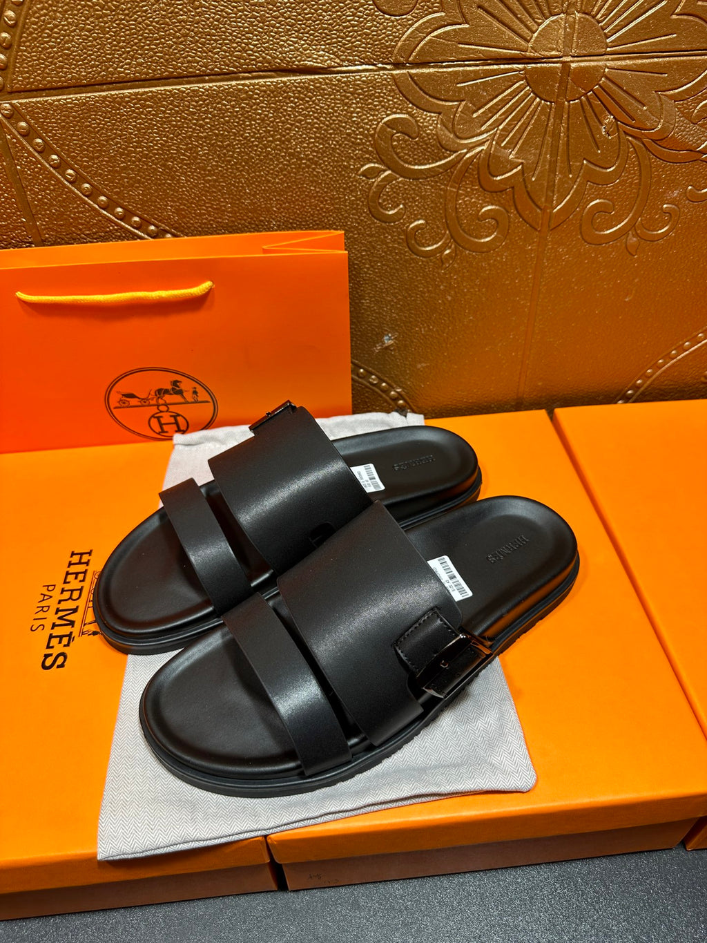 Black leather slide sandals with double strap and buckle, side view on dust bag