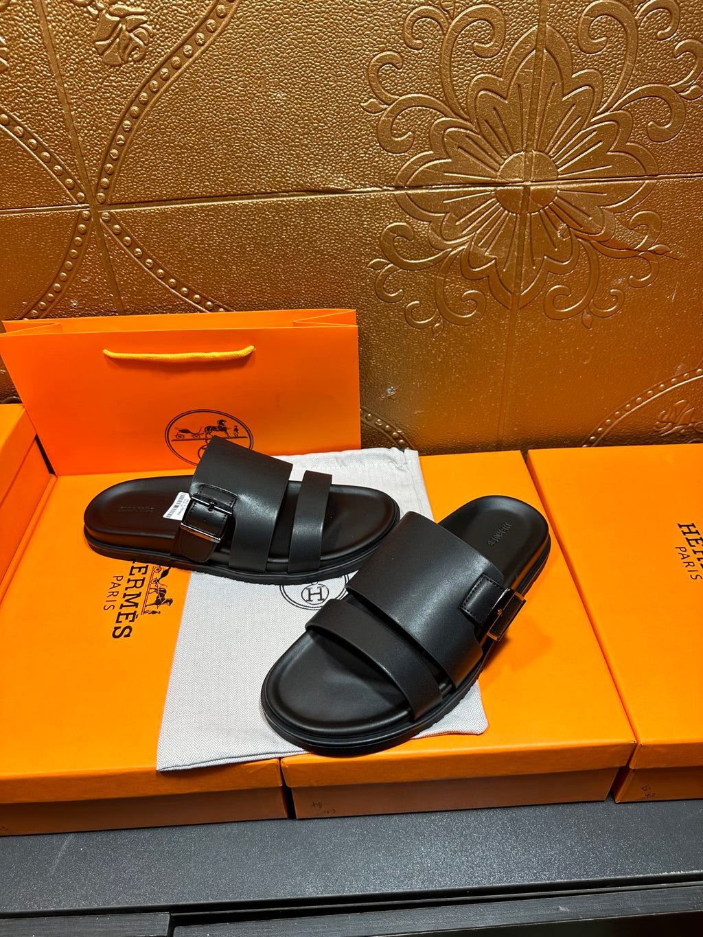 Black leather slide sandals with wide buckled straps, pair on dust bag and box