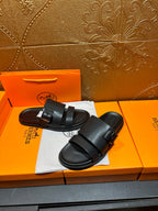 Black leather slide sandals with wide buckled straps, pair on dust bag and box
