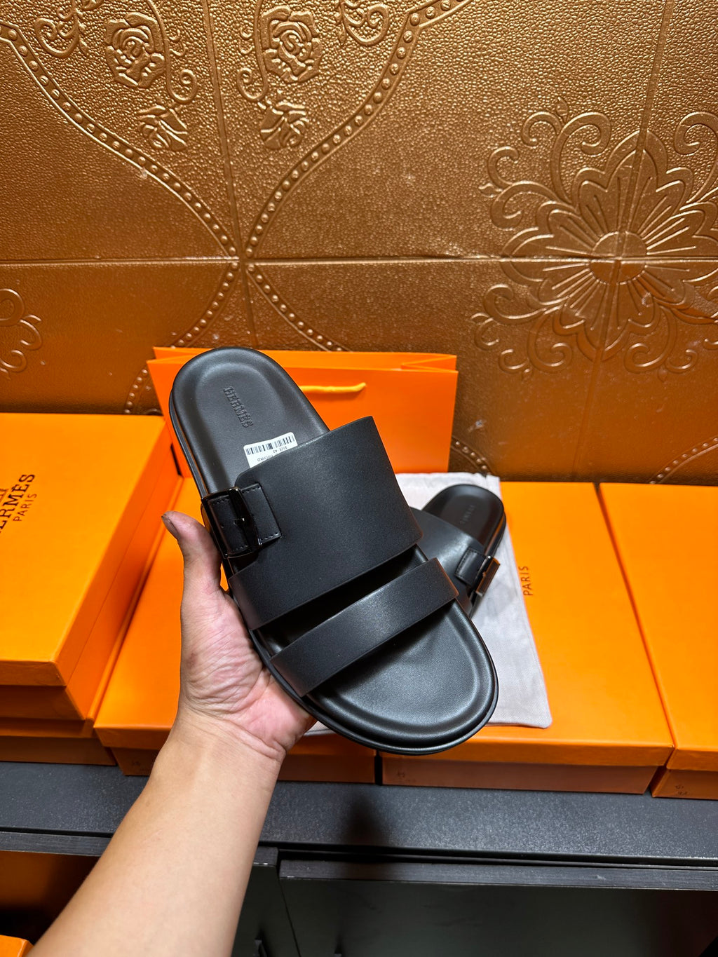 Black leather slide sandals with wide straps and buckle, held up for close view