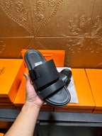 Black leather slide sandals with wide straps and buckle, held up for close view