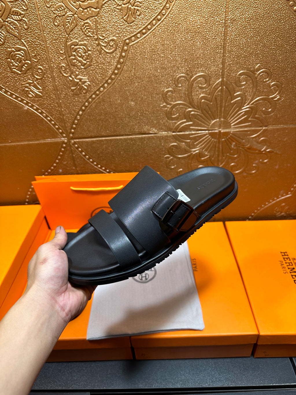 Black leather slide sandals with double buckle strap, held in hand