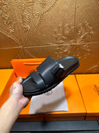 Black leather slide sandals with double buckle strap, held in hand