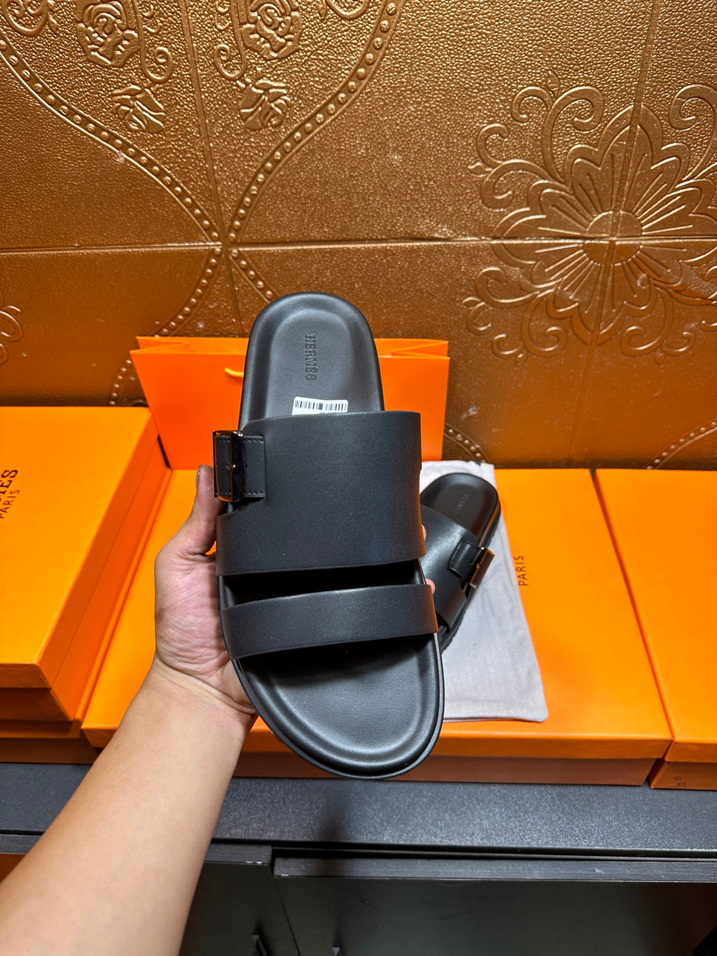 Black leather slide sandals with buckled strap, side view held up
