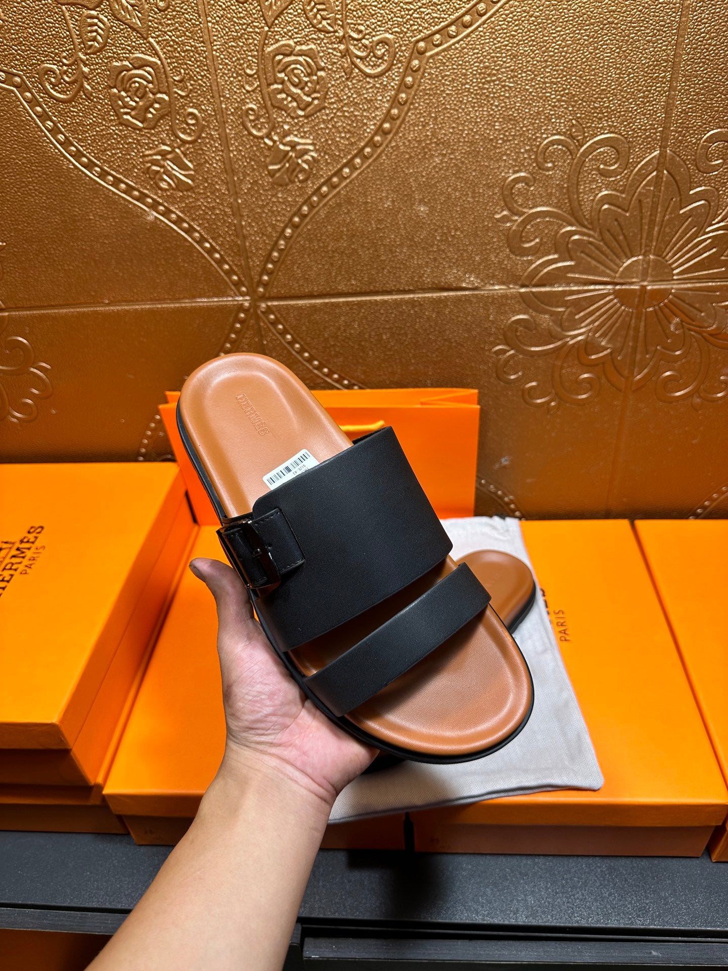 Hermes leather sandals held in hand, black straps with adjustable buckle and tan sole