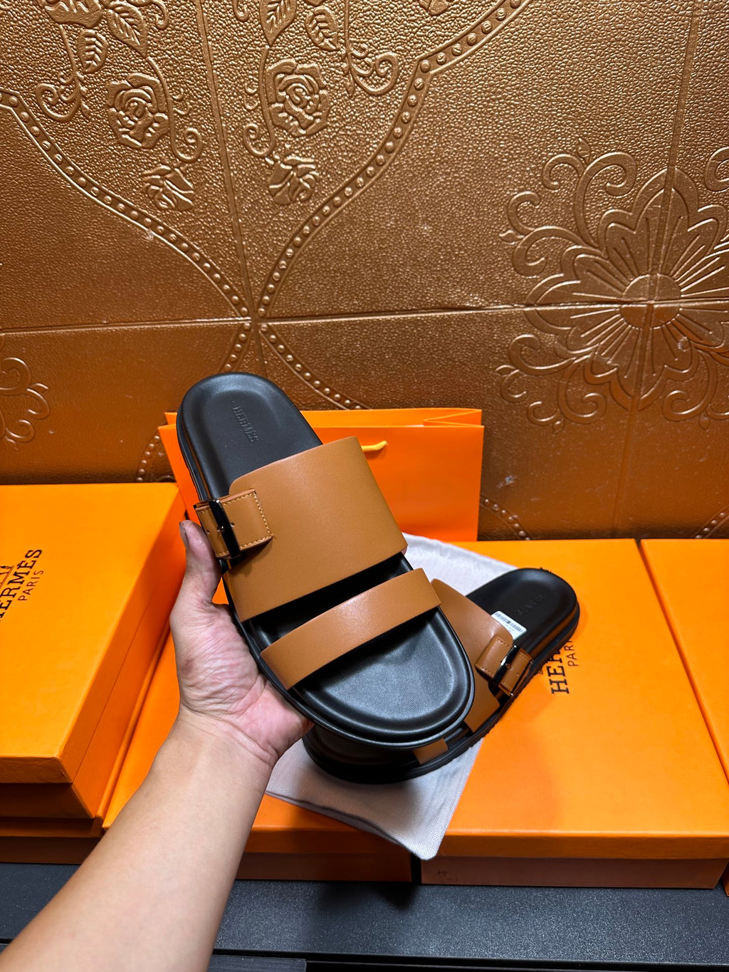 Tan and black Hermes slide sandals front view being held