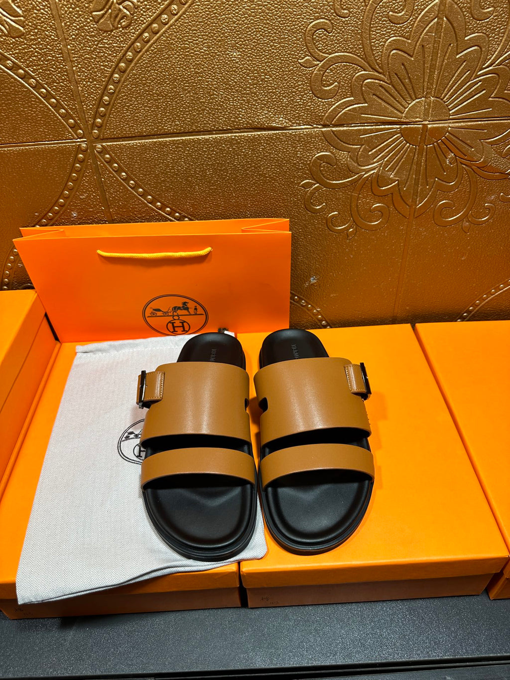 Tan and black Hermes slide sandals with two-strap buckle design