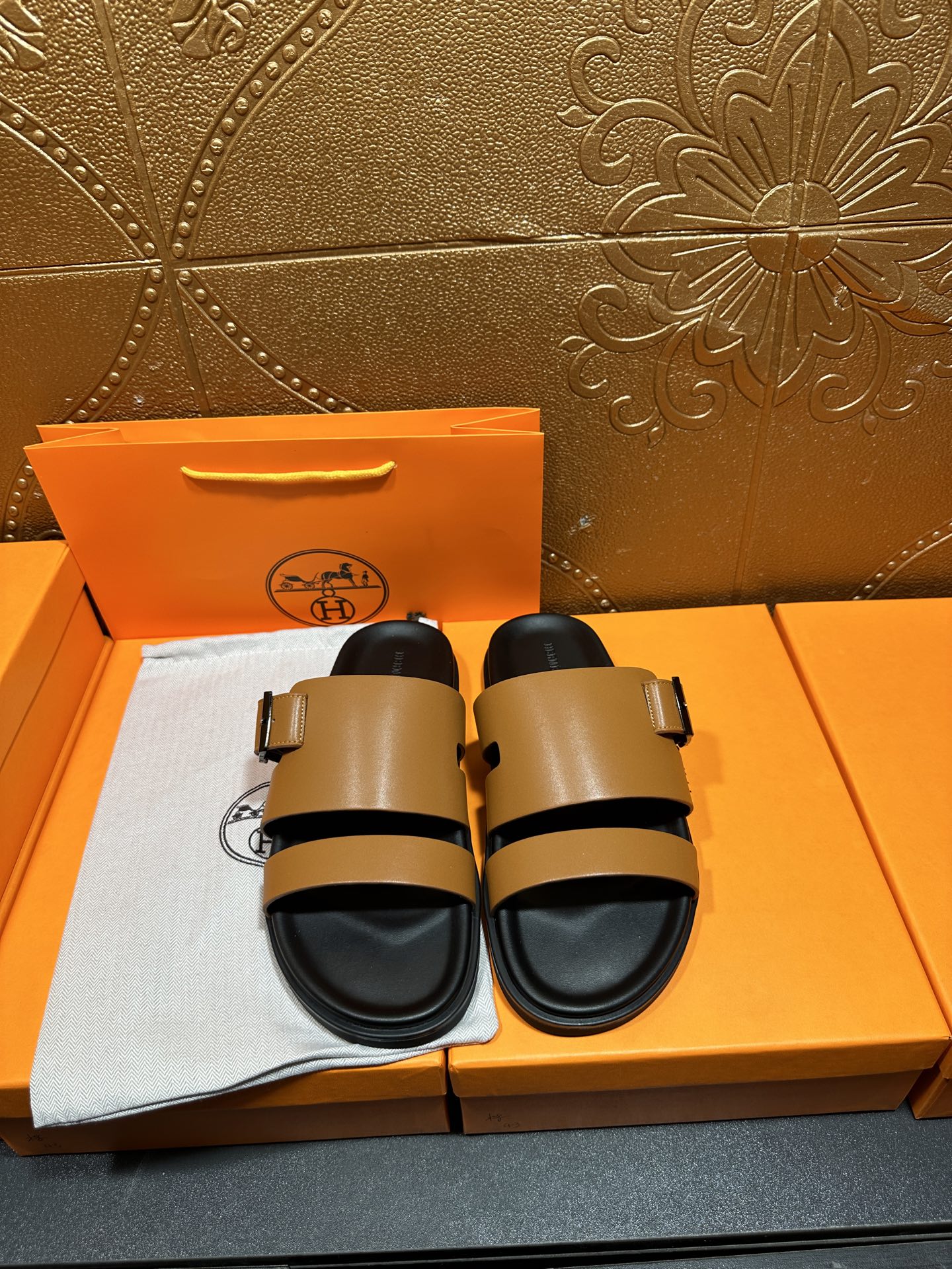 Tan and black Hermes slide sandals with two-strap buckle design