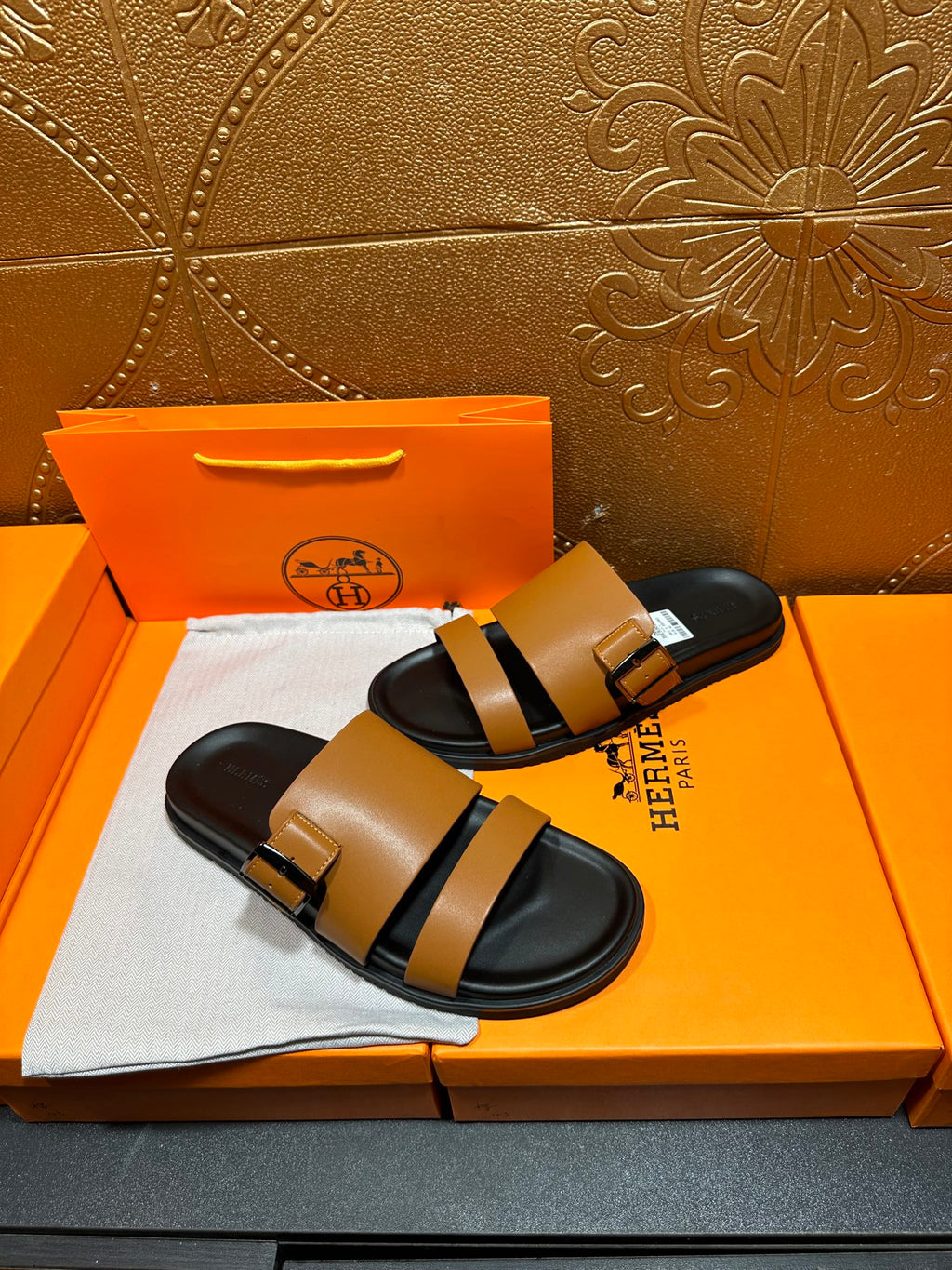 Tan and black Hermes slide sandals with HERMES tag on footbed