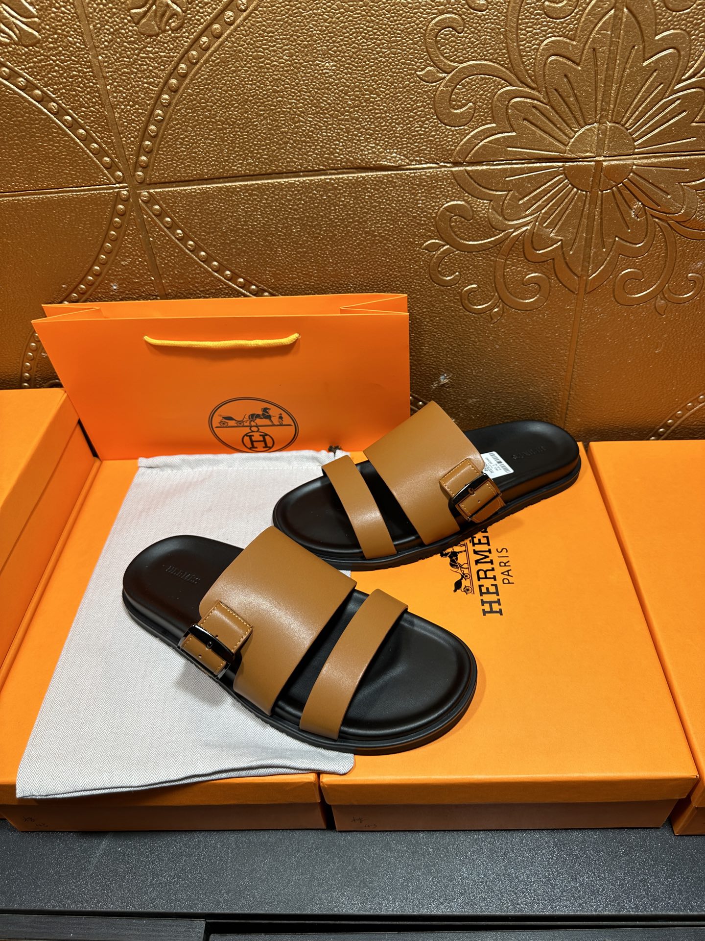 Tan and black Hermes slide sandals with HERMES tag on footbed