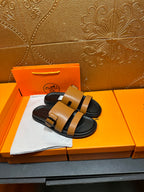 Tan and black Hermes slide sandals laid on orange box padding