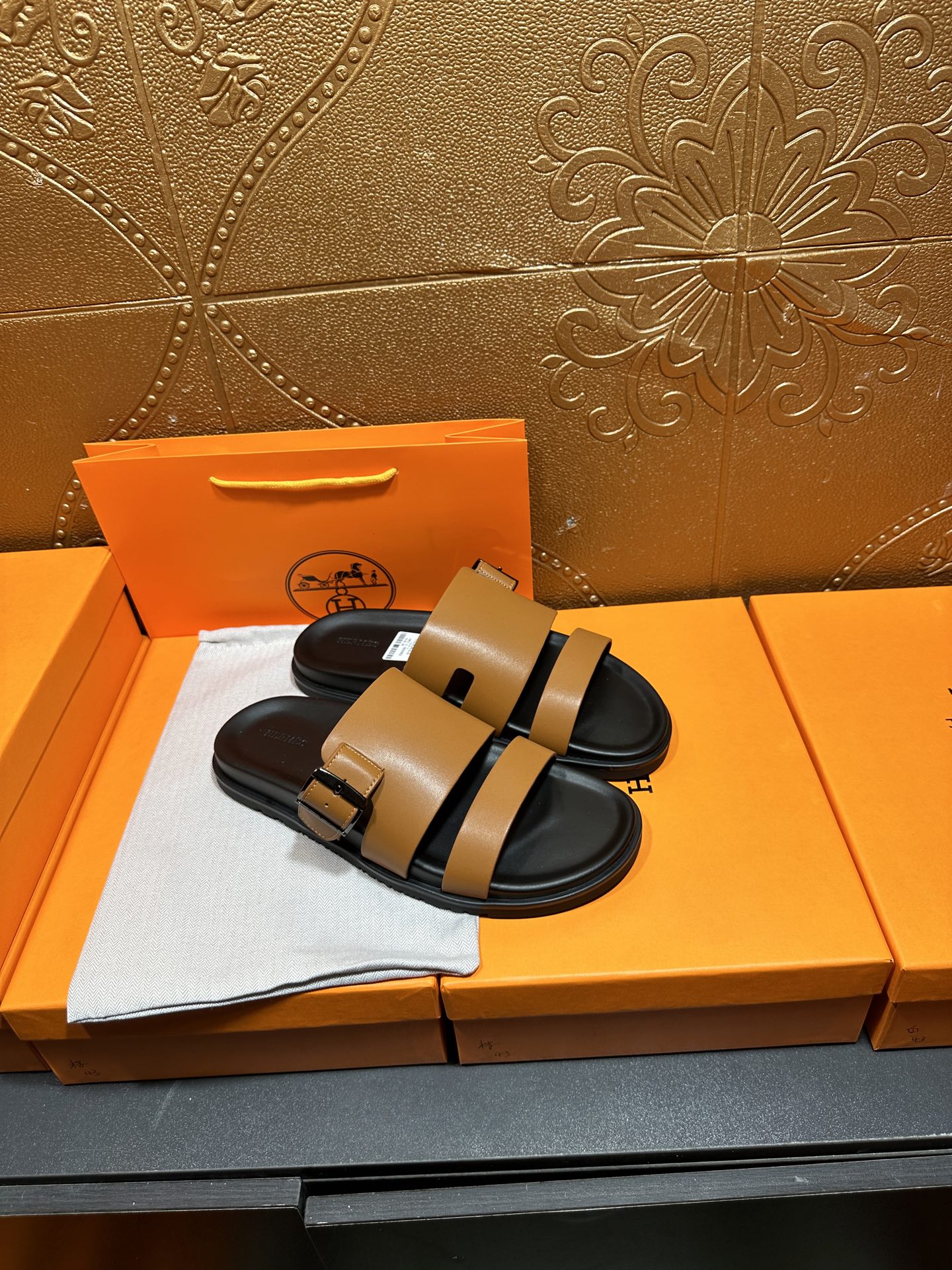 Tan and black Hermes slide sandals laid on orange box padding