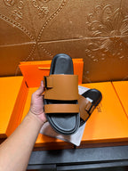 Tan and black Hermes slide sandals held with one strap and buckle visible