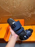 Hermes dark blue slide sandals held in hand, showing double strap design.