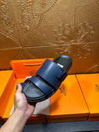 Hermes dark blue sandals held up, showing top straps and textured footbed.