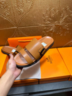 Tan leather slide sandals held in hand, two buckle straps and black-trimmed sole