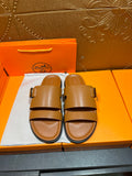 Tan leather slide sandals with two buckle straps and black rubber footbed edge