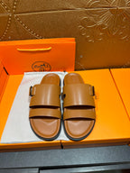 Tan leather slide sandals with two buckle straps and black rubber footbed edge