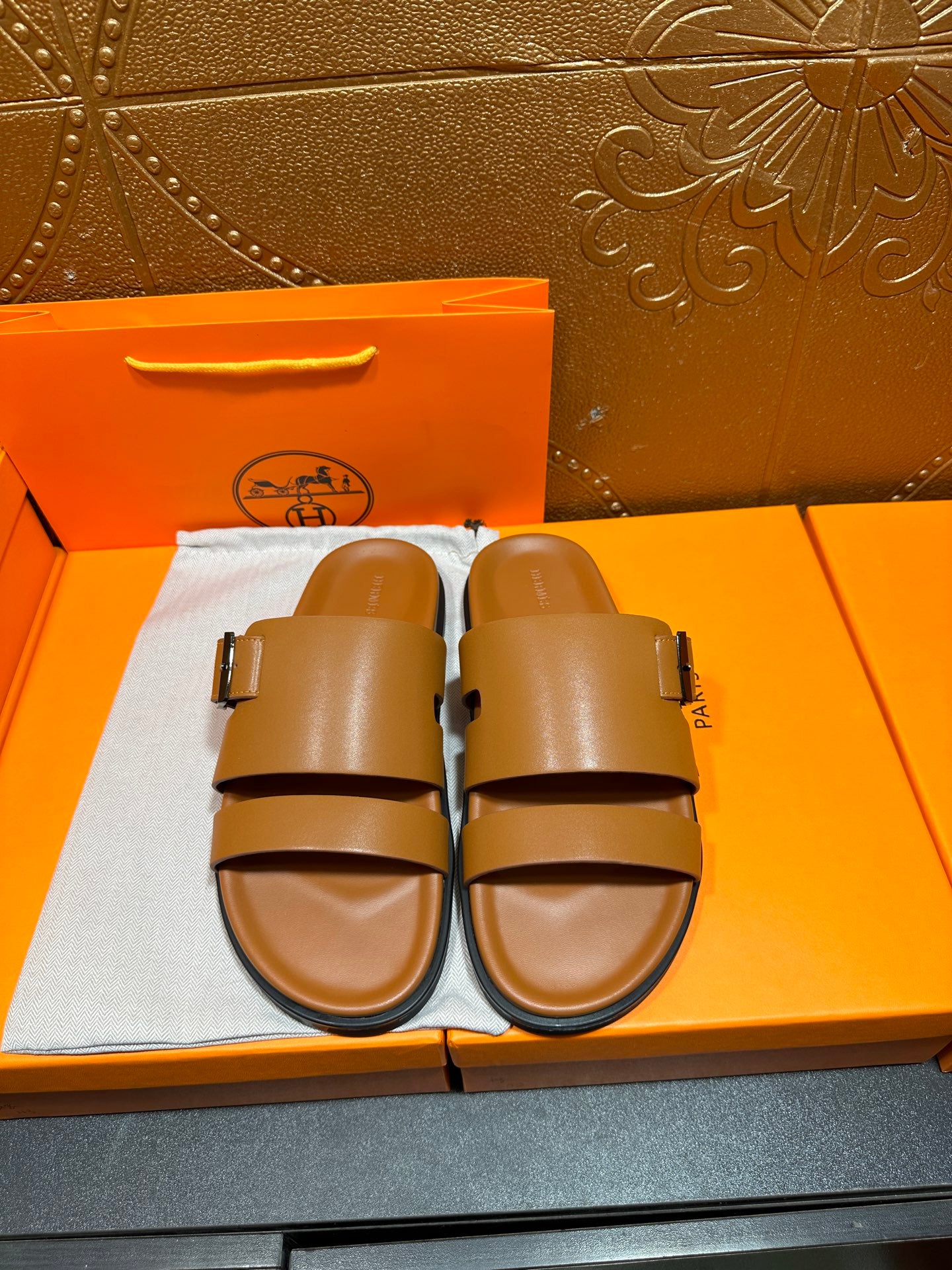 Tan leather slide sandals with two buckle straps and black rubber footbed edge