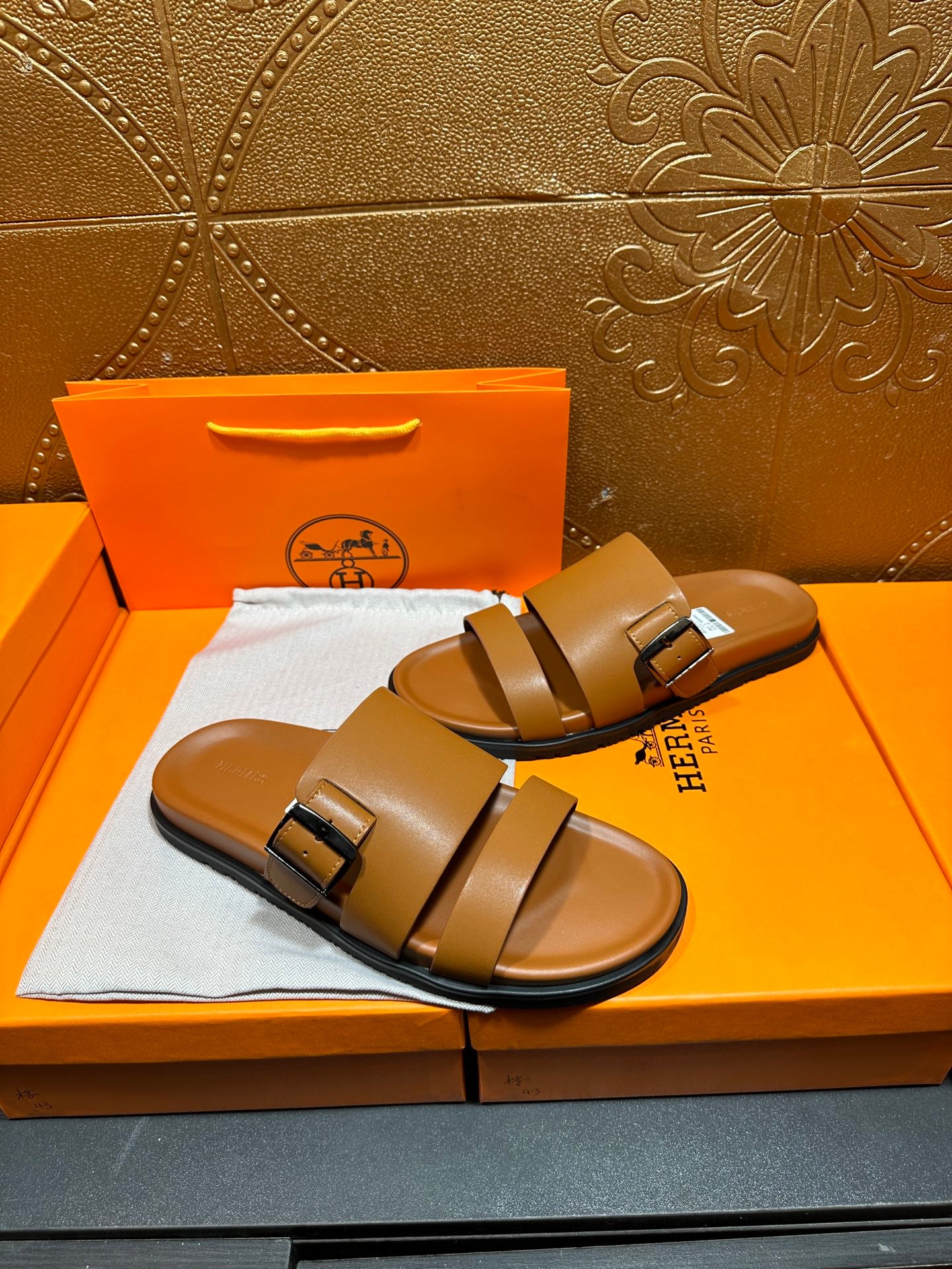 Tan leather slide sandals with two buckles and curved footbed, angled view