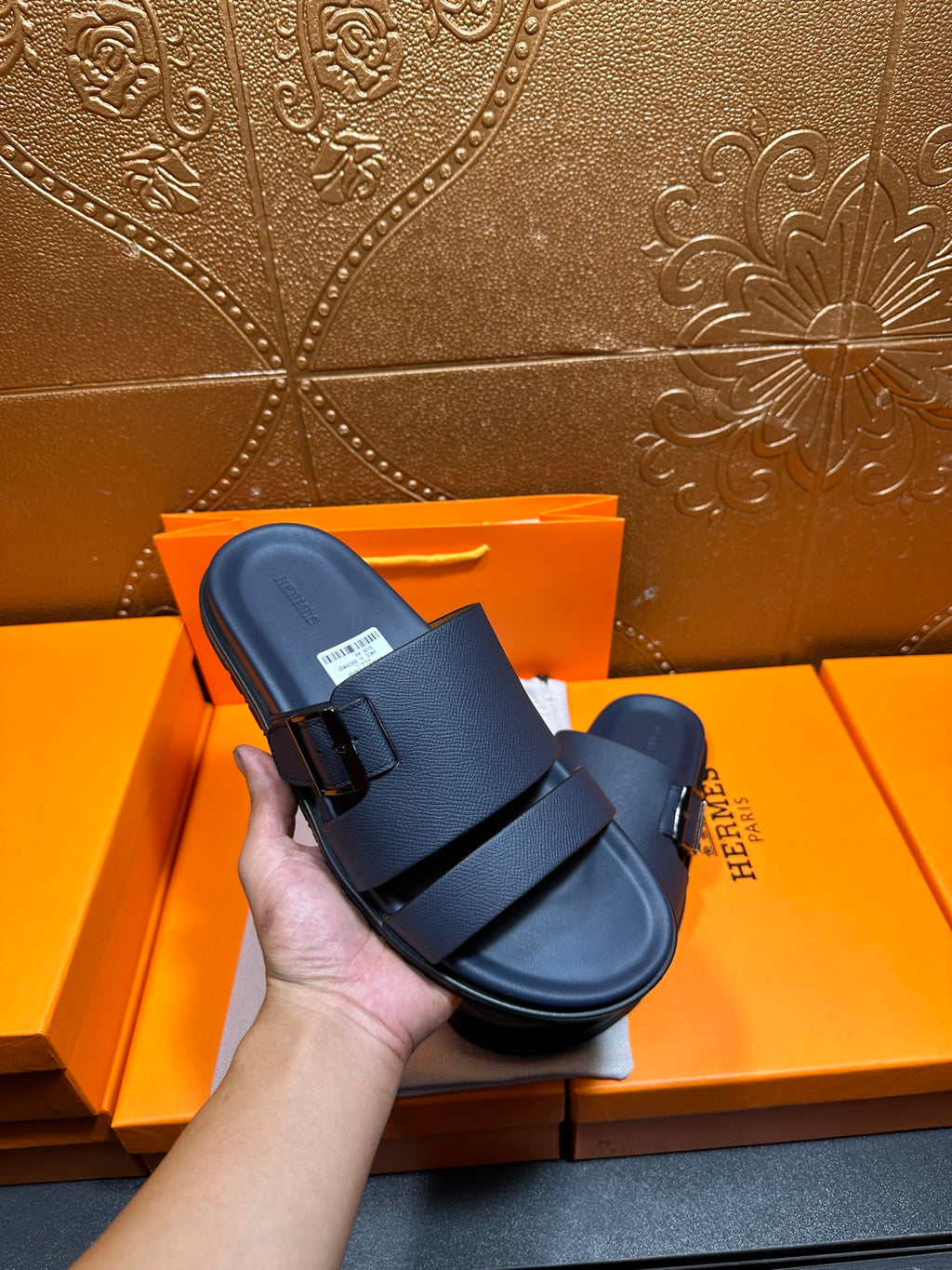 Blue slide sandals with two buckled straps, held in hand above box