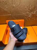 Blue slide sandals with two buckled straps, held in hand above box