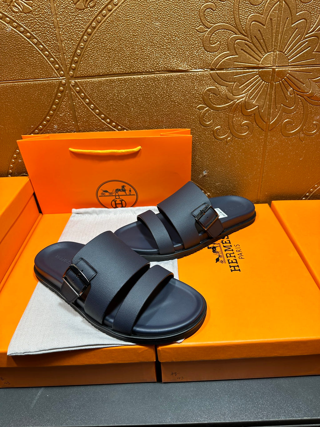 Blue slide sandals with two adjustable buckle straps, side view on box