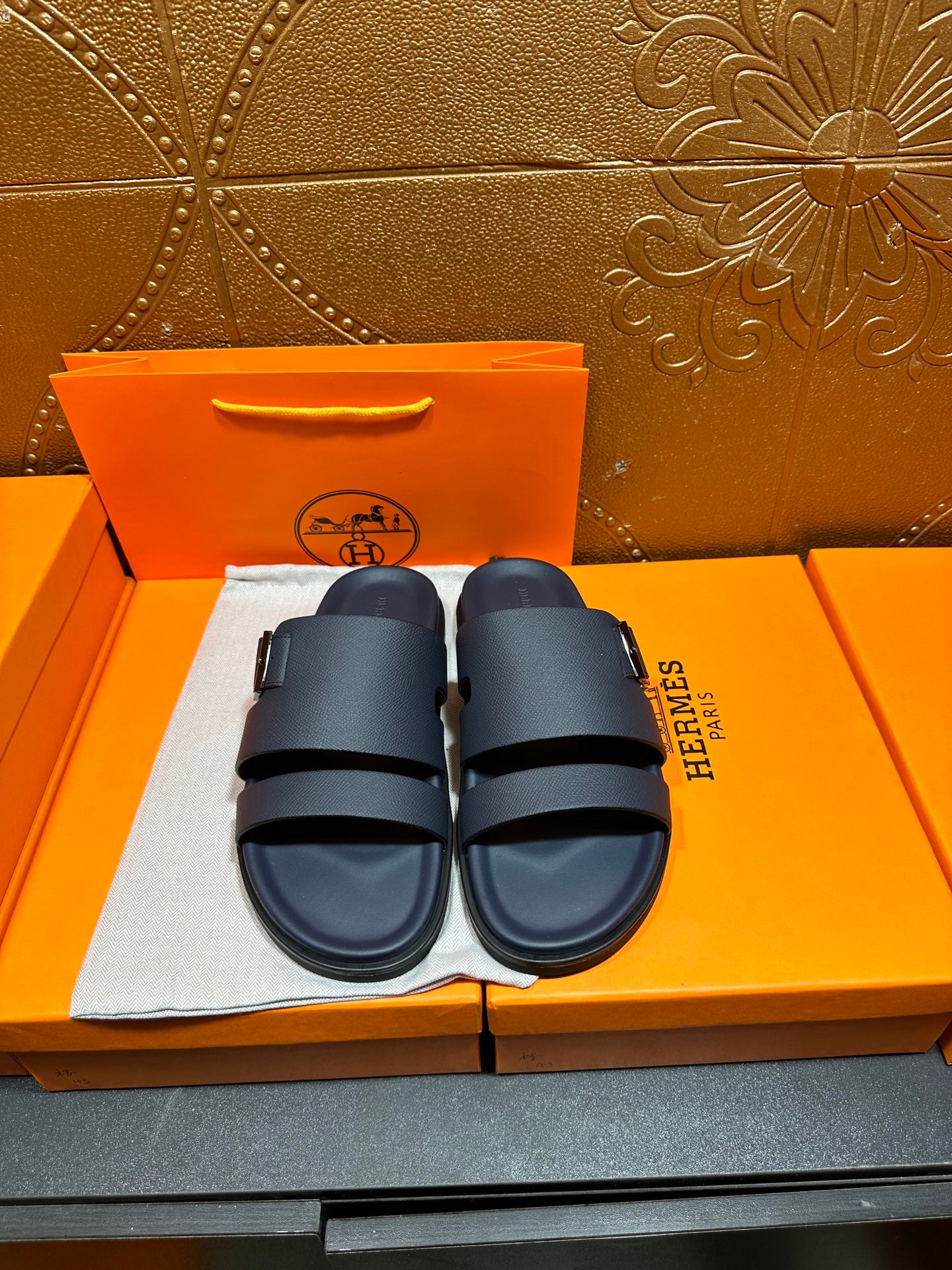 Blue slide sandals with two buckled straps, shown on a box set