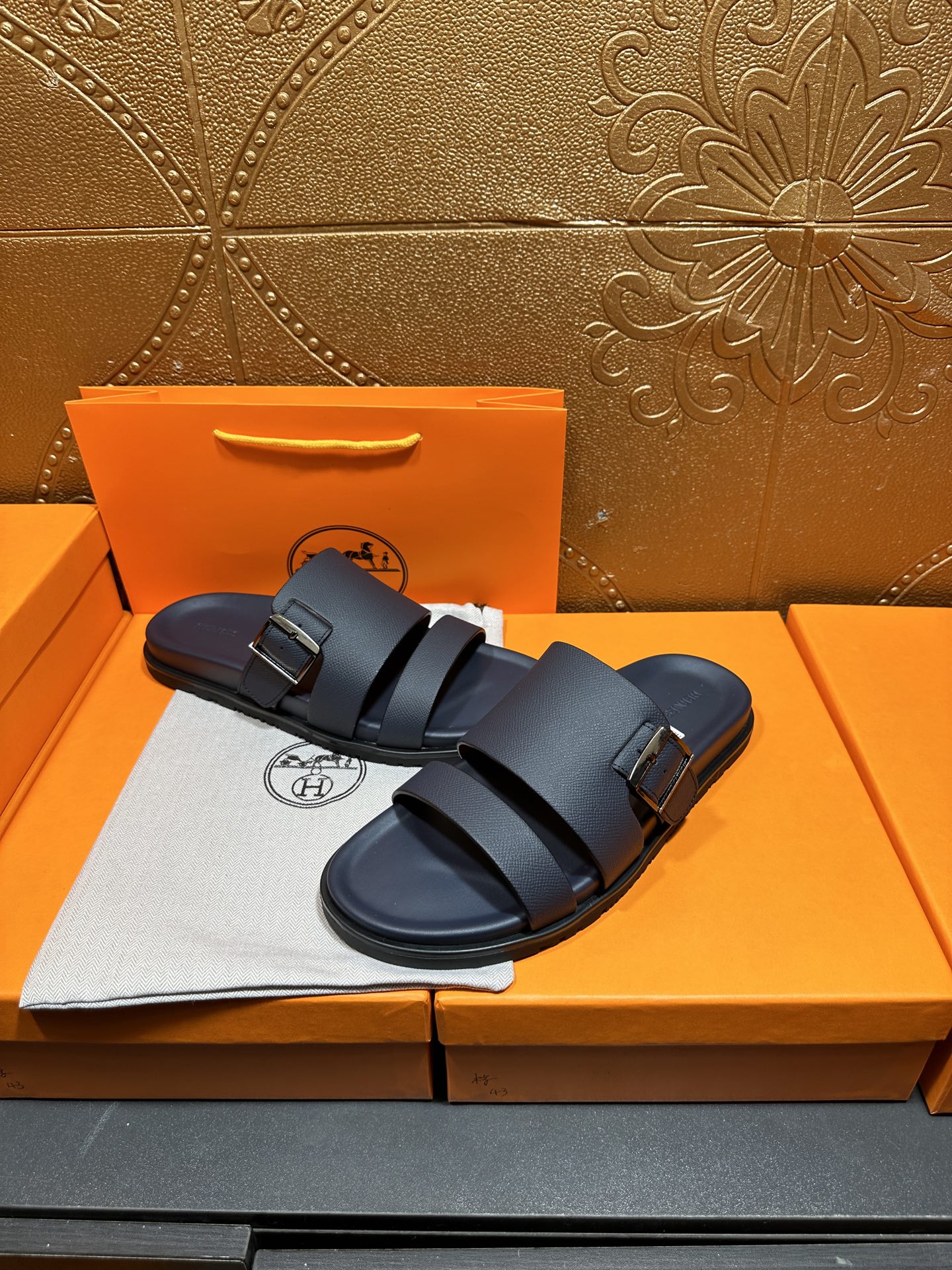 Blue leather slide sandals with double buckled straps, resting on box
