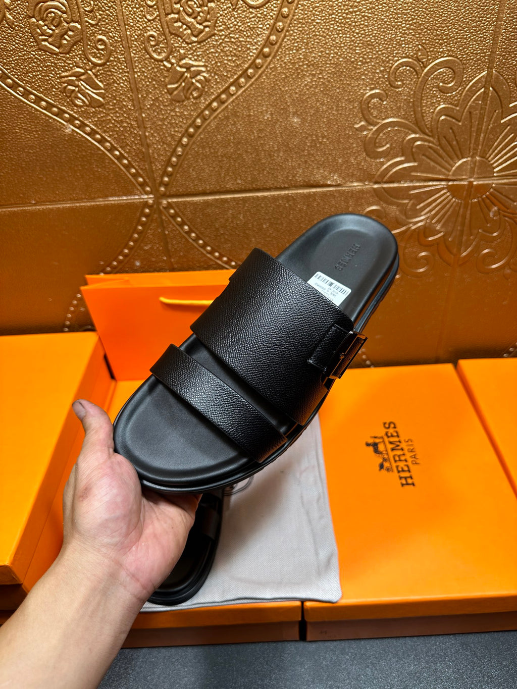 Hermes black slide sandals held in hand over shoebox, thick textured straps