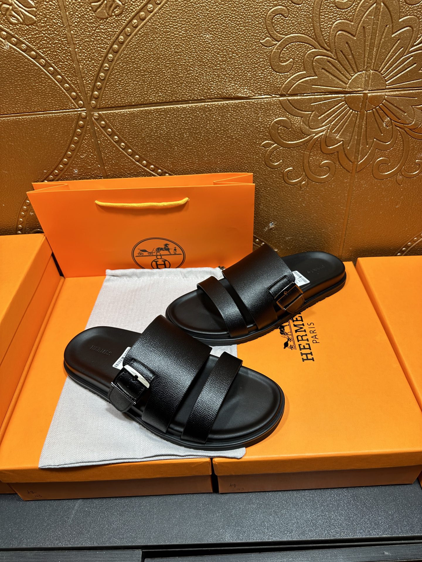 Hermes black slide sandals with double straps, side view on shoebox
