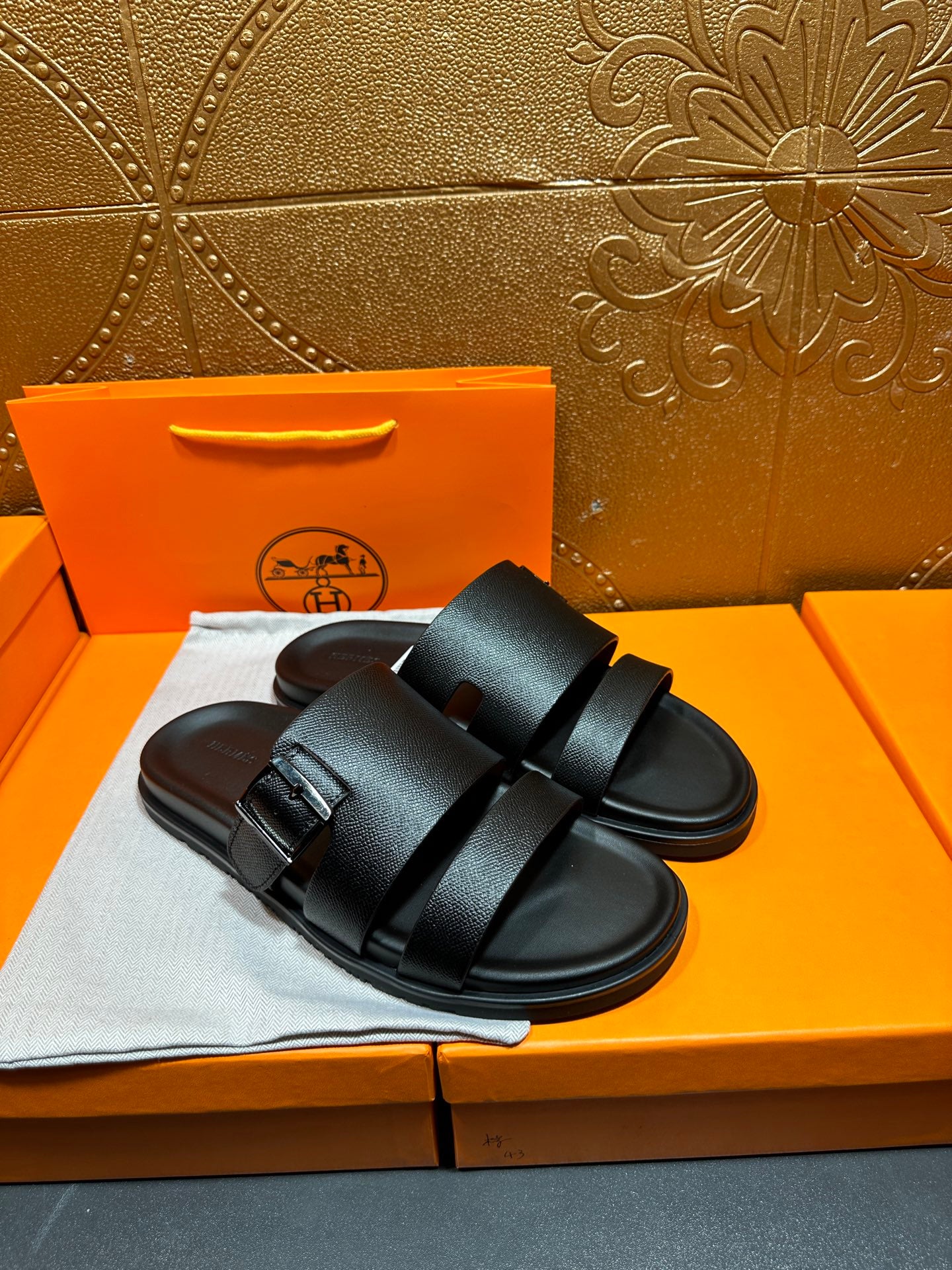 Hermes black slide sandals with double straps, front view on shoebox