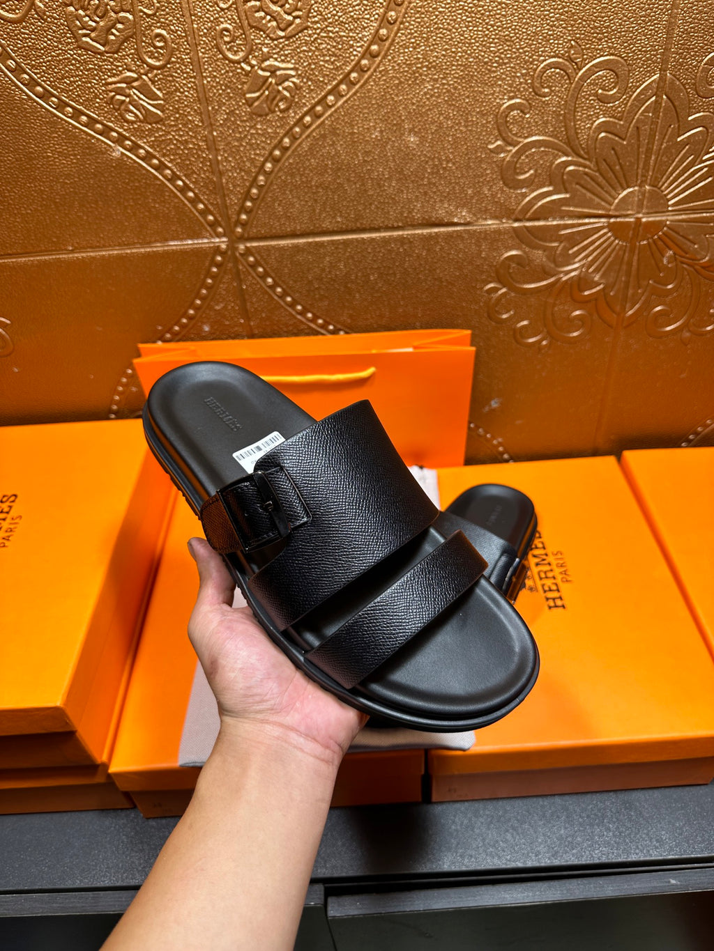 Hermes black slide sandals held in hand, double strap across the top